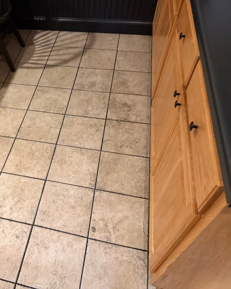 Dirty tile floor beside the cabinets in an office break room before cleaning in Lawrenceville, GA